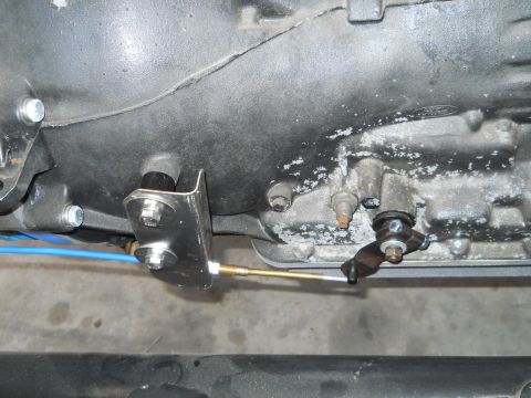 1992 Ford Bronco - Close-up view of a transmission shift linkage mechanism, a blue cable and a metal bracket attached to the transmission housing.