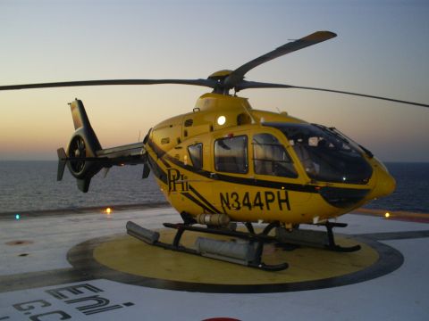 1992 Ford Bronco - A yellow helicopter sits on a helipad near the ocean at sunset.