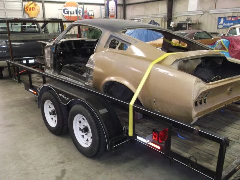 1967 Ford Mustang - A classic car body, likely a Ford Mustang, is being transported on a trailer in a workshop.