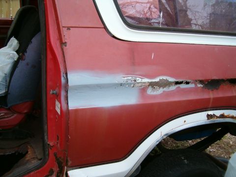 1979 Ford Bronco - Side view of a red SUV door with significant rust and primer patches.