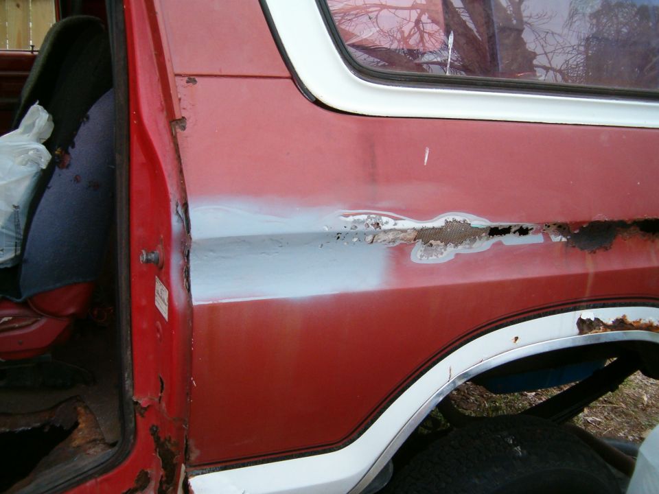 Red SUV door showing rust damage and primer spots. Interior seat visible