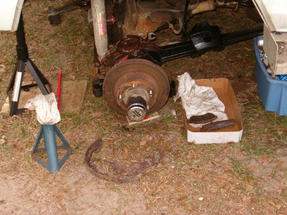 Rusty five-lug drum brake exposed under a jacked-up truck with jack stands and removed parts on grass