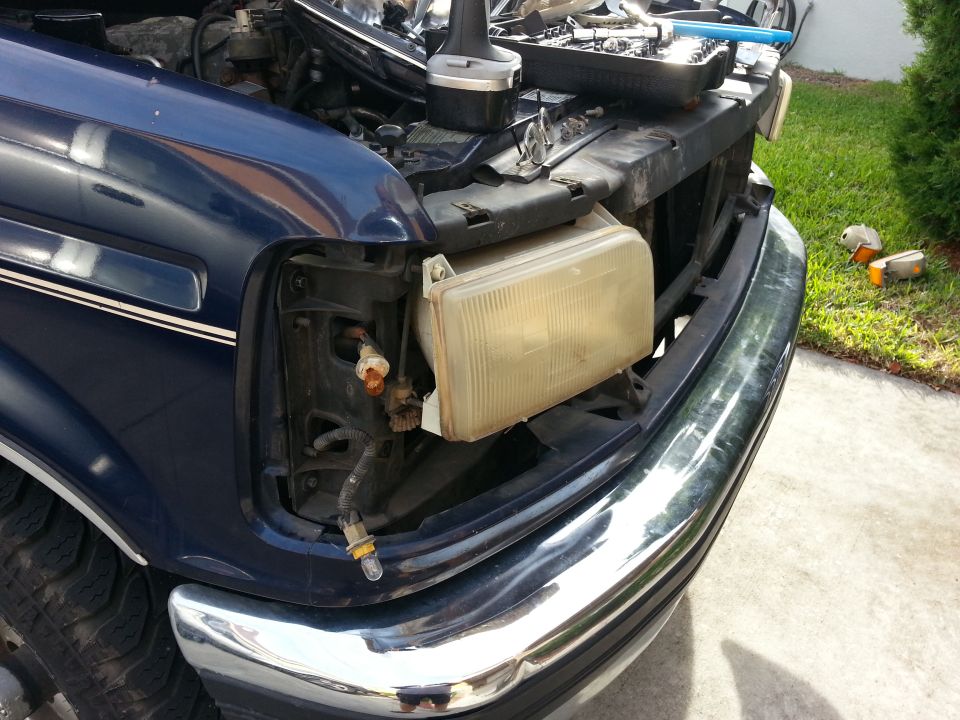 Blue Ford truck front end with headlight removed, chrome bumper, and open hood