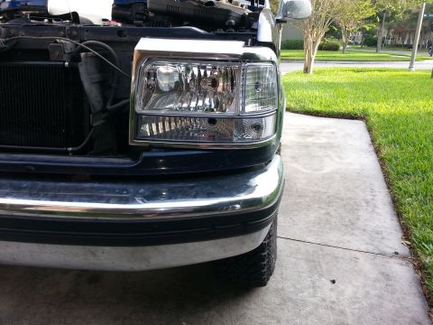 1994 Ford Bronco - The front passenger side headlight assembly of a dark-colored vehicle is shown in this close-up shot.
