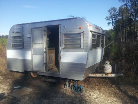 1986 Ford Bronco - A vintage silver travel trailer sits outdoors with its door ajar and a propane tank on the tongue.