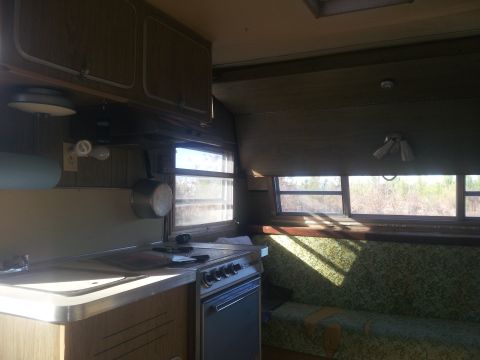 1986 Ford Bronco - The interior of a vintage camper shows a compact kitchen area and a seating area with a view of the outdoors.