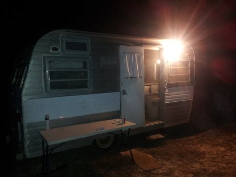 1986 Ford Bronco - A vintage camper trailer is parked outside at night, with its door open and a bright light illuminating the entrance.