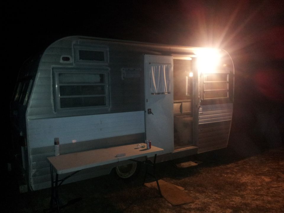 side view of a vintage camper trailer at night with the door open and a light on