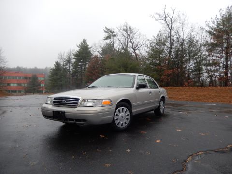 2001 Ford Crown Victoria - A silver 2001 Ford Crown Victoria sedan is parked on a wet asphalt lot with trees in the background.
