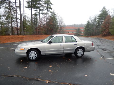 2001 Ford Crown Victoria - A silver sedan is parked on a wet asphalt lot with fallen leaves scattered around.