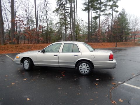 2001 Ford Crown Victoria - A silver 2001 Ford Crown Victoria sedan is parked on a wet asphalt lot surrounded by trees in autumn.