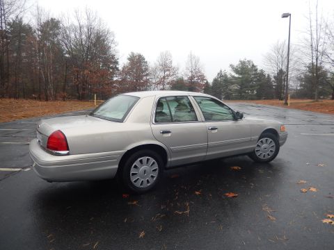 2001 Ford Crown Victoria - A silver 2001 Ford Crown Victoria sedan is parked outdoors on a wet asphalt surface with fallen leaves scattered around.