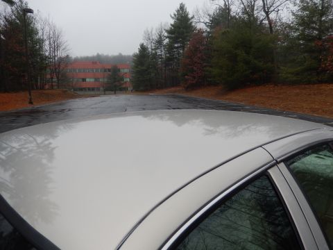 2001 Ford Crown Victoria - A view from above a car's roof shows a wet parking lot and a building surrounded by trees.