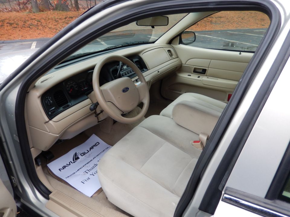 2001 Ford Crown Victoria interior showing tan seats, dashboard, and steering wheel. Floor mat has a NaviGuard paper