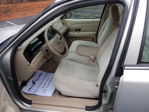 2001 Ford Crown Victoria - The interior of a 2001 Ford Crown Victoria, tan cloth seats and a tan dashboard, is visible through the open passenger door.