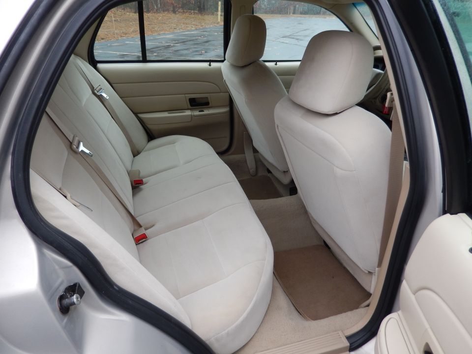 Tan cloth interior of a 2001 Ford Crown Victoria, showing the rear bench seat, front seats, and door panel