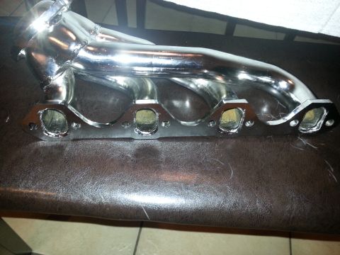 1994 Ford Bronco - A shiny chrome exhaust manifold is displayed on a brown textured surface.