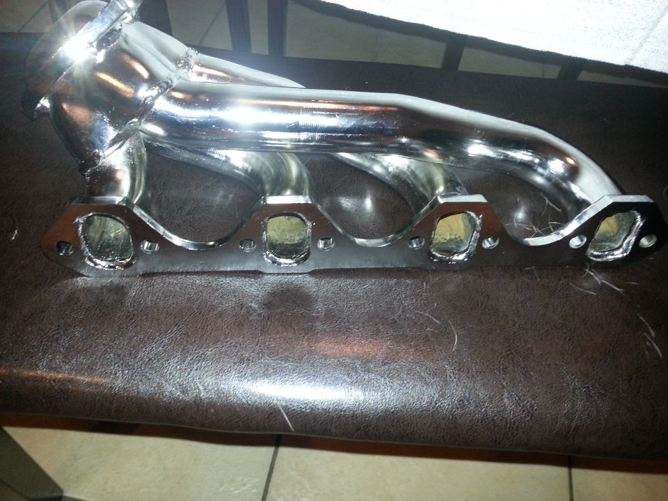Chrome exhaust manifold with four ports on a brown surface