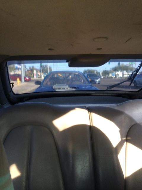 1995 Ford Probe - View through rear window of a blue car with a prominent hood scoop, seen from the interior of another vehicle.