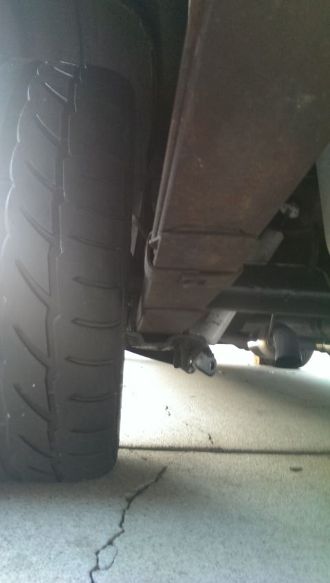 1987 Ford Bronco - The underside of a vehicle shows a tire and rusty leaf spring assembly.