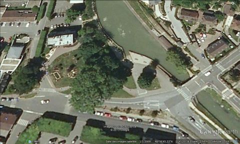 1991 Ford LTD Crown Victoria - Aerial view of a town with a canal, showing buildings, trees, and roads with parked and moving vehicles.