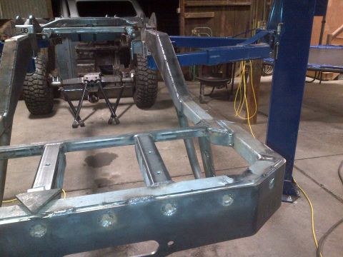 1985 Jeep CJ7 - The bare frame of a Jeep CJ is shown in a workshop, undergoing modifications or repairs.