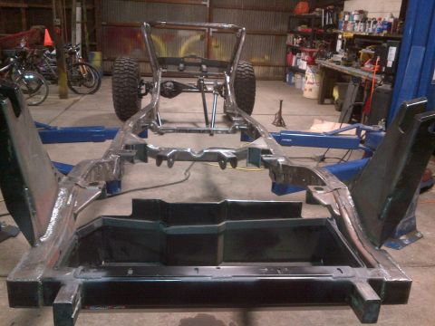 1985 Jeep CJ7 - The bare frame of a Jeep CJ is elevated on a lift, showing its chassis and suspension components.