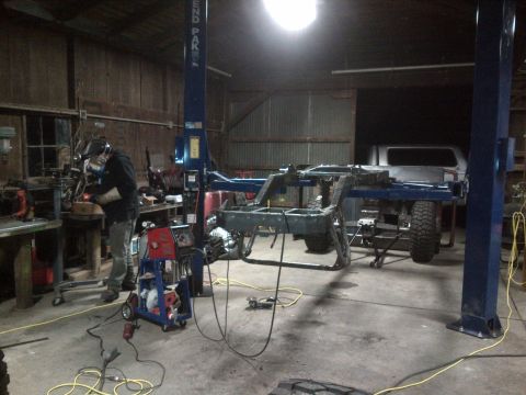 1985 Jeep CJ7 - A workshop scene shows a Jeep CJ frame being worked on, with a welder and a pickup truck present.