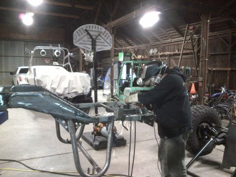 1985 Jeep CJ7 - Man welding a vehicle frame in a workshop with other vehicles present.