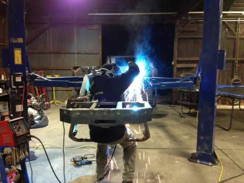 1985 Jeep CJ7 - A person is welding a vehicle frame that is suspended on a lift in a workshop.
