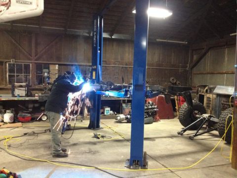 1985 Jeep CJ7 - A person welds on a Jeep CJ frame and drivetrain assembly in a workshop.