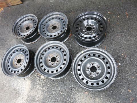 2001 Ford Crown Victoria - A collection of six used steel wheels are displayed on a paved surface.