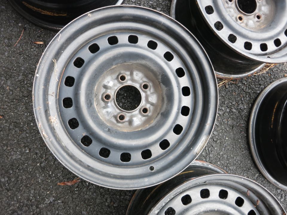 Several steel wheels with square holes are stacked on asphalt