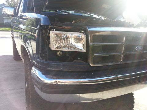 1994 Ford Bronco - The front driver side headlight assembly of a dark green 1992 Ford Bronco is shown removed from the vehicle.