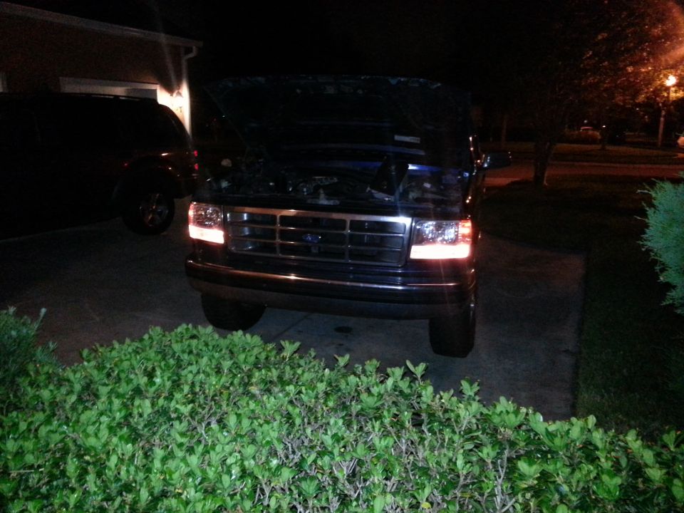 1992 Ford Bronco front view, hood open, parked in driveway at night. Another dark SUV is parked to the left