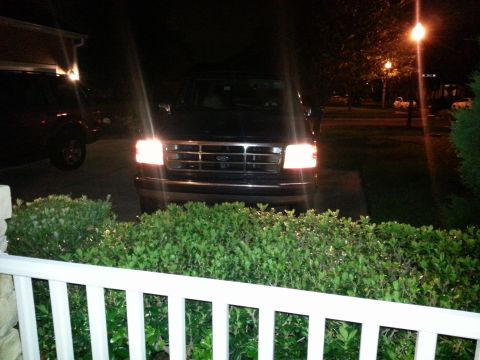 1994 Ford Bronco - A dark Ford F-Series truck is parked at night with its headlights illuminated, with another vehicle nearby.