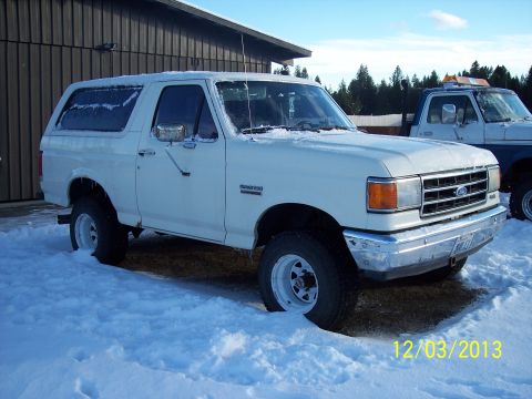 1990 Ford Bronco - A white Ford Bronco sits in the snow outside a building, with another truck visible in the background.