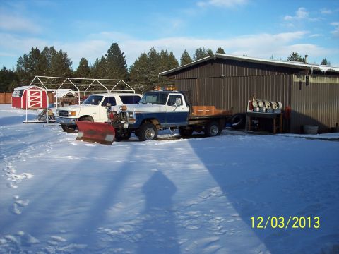 1973 Ford F-250 - Two trucks, one a 1973 Ford F-250 with a plow, sit parked in the snow near a building.