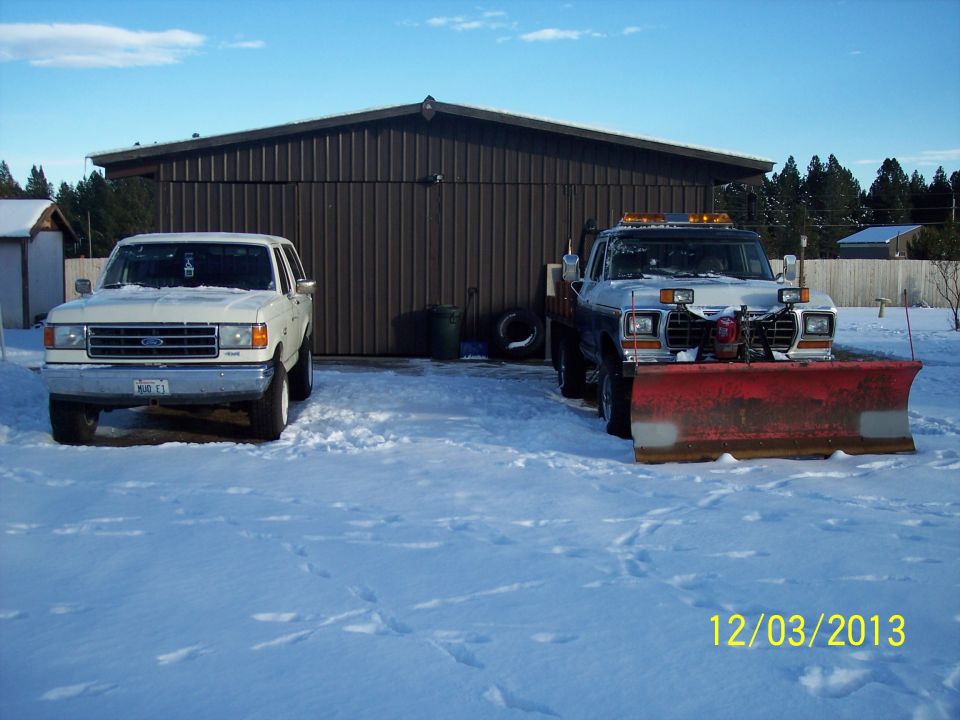 Two white Ford trucks parked in snow, one with a snow plow