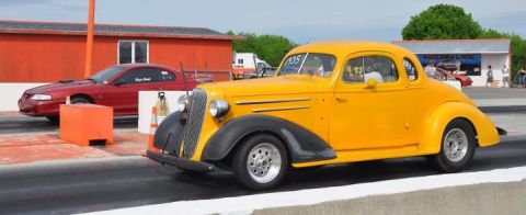 1935 Chevrolet New - A yellow 1935 Chevrolet coupe is on a drag strip next to a red Ford Mustang.