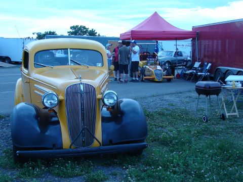 1935 Chevrolet New - A yellow and black 1935 Chevrolet truck is parked at an outdoor event with people and other vehicles in the background.
