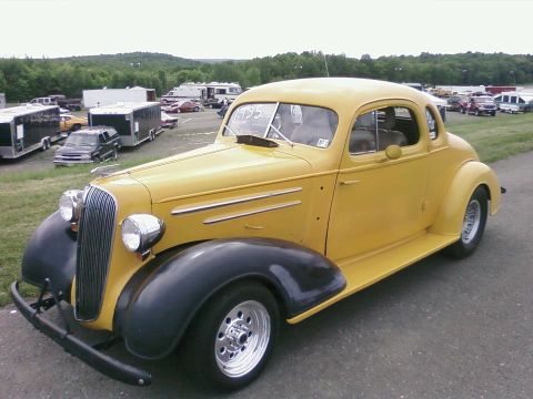 1935 Chevrolet New - A yellow coupe with a distinctive grille and chrome wheels sits parked outdoors.