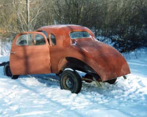 1935 Chevrolet New - A red 1935 Chevrolet coupe sits in the snow with its doors open, appearing to be in a state of restoration or disrepair.