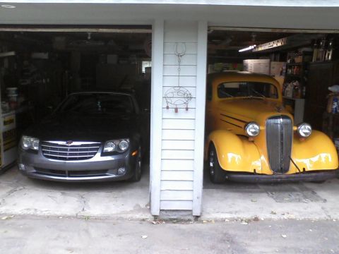 1935 Chevrolet new - Two vehicles are parked in a garage, one a yellow vintage truck and the other a modern dark sedan.