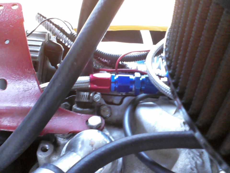 Engine bay with red bracket, blue and red fuel line fittings, and air filter