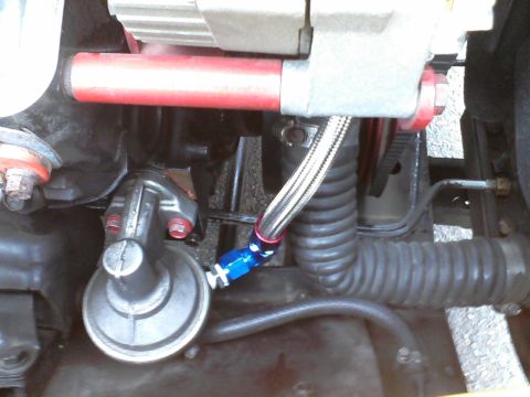 1935 Chevrolet new - Close-up view of an engine component, likely a fuel pump, with braided fuel lines and a red metal bar.
