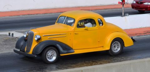 1935 Chevrolet new - A yellow 1935 Chevrolet coupe hot rod is seen on a race track with another vehicle in the background.