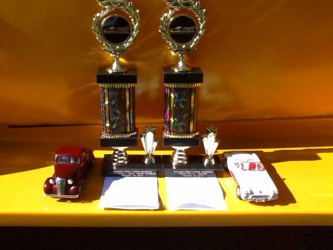 1935 Chevrolet new - A display two toy cars and two trophies, possibly from a car show or event.