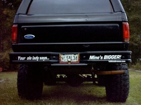1995 Ford Bronco - Rear view of a black Ford Bronco with custom bumper text and large off-road tires.