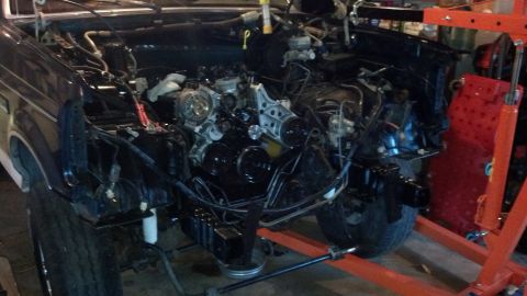 1993 Ford Bronco - Vehicle engine bay is open, with the engine removed and supported by an engine hoist, indicating a rebuild or repair process.